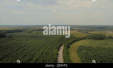 Asphalt road between forest and rural fields in Ural, Russia. Beautiful summer nature landscape at during daytime. Aerial view from a drone Stock Photo