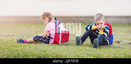 A boy and a girl quarreling and are sitting on the grass in the schoolyard back to back Stock Photo