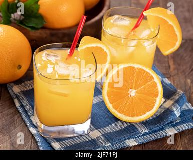 Glass of cold orange juice and sliced oranges on a wooden table with bowl of oranges in background Stock Photo