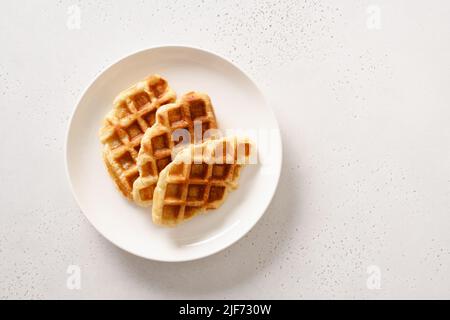 Trendy delicious croffles on white plate on a white background. Croissant as waffle. View from above. Copy space. Stock Photo