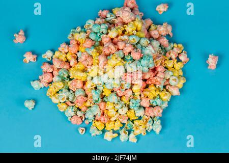 Multi-colored popcorn is scattered on a blue background. Colorful beautiful sweet dessert. Stock Photo