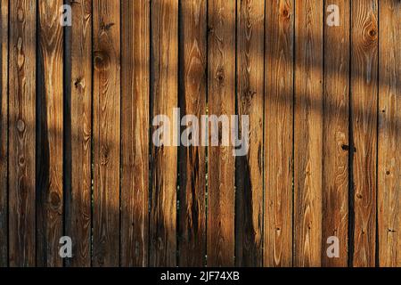 Brown wooden fence texture with shadows in evening sunlight. Background of wooden planks. Stock Photo