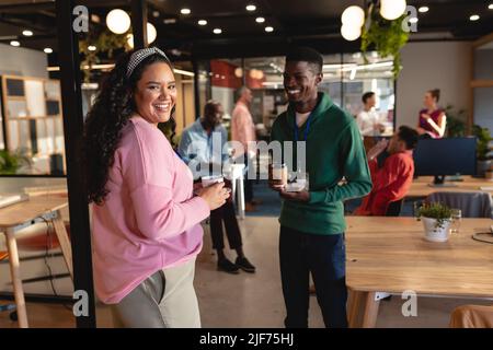 Smiling multiracial colleagues discussing while having coffee during break in office Stock Photo