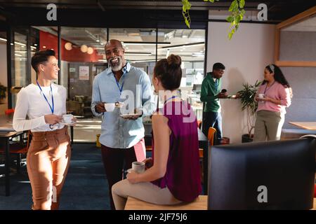 Happy multiracial colleagues discussing while having coffee in office Stock Photo