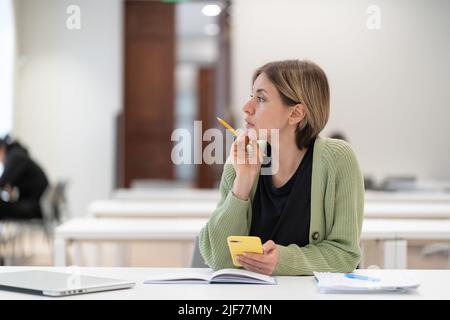 Mature female student taking second degree looking through window and dreaming, studying in library Stock Photo