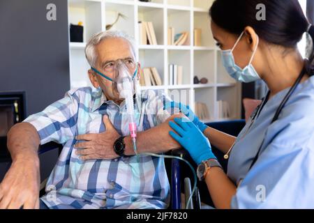Biracial female health worker helping caucasian senior man to use oxygen mask at home Stock Photo