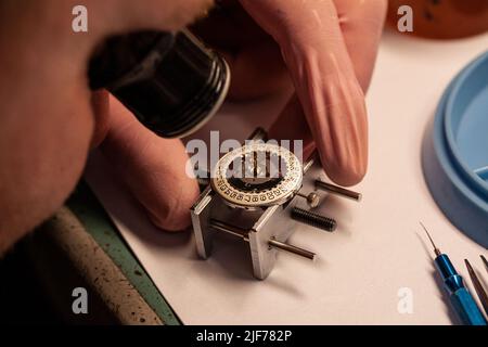 Watch repair at watchmaker wiyh magnifying glass. Focus on date disc inside case. Maintenance of clockwork. Selective focus close-up image. Stock Photo