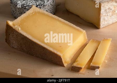 Piece of  French Abondance cheese and slices on a cutting board close up Stock Photo