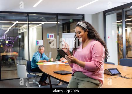 Smiling young biracial businesswoman using tablet pc while colleagues in background Stock Photo