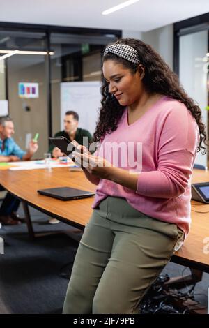 Smiling young biracial businesswoman using tablet pc while colleagues in background Stock Photo