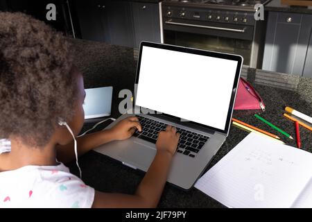 African american girl wearing headphones studying over laptop on table at home, copy space Stock Photo