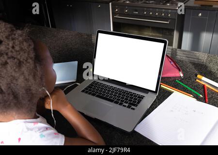 African american girl wearing headphones attending online lecture over laptop on table at home Stock Photo