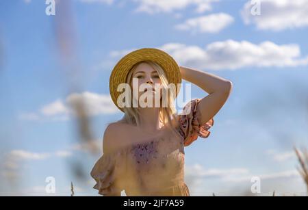 Portrait of a beautiful young woman in a straw hat against a blue sky background. Smiling young girl poses for the camera. Stock Photo