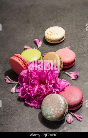 Macarons with peony flower on a stone background. Sweet dessert, colorful and pastel colors. Romantic style, festive card, flat lay, hard light, dark Stock Photo
