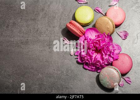 Macarons with peony flower on a stone background. Sweet dessert, colorful and pastel colors. Romantic style, festive card, flat lay, hard light, dark Stock Photo
