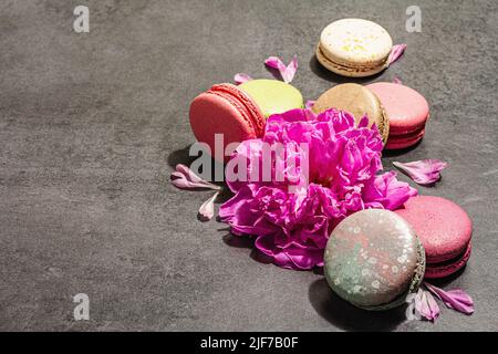 Macarons with peony flower on a stone background. Sweet dessert, colorful and pastel colors. Romantic style, festive card, flat lay, hard light, dark Stock Photo
