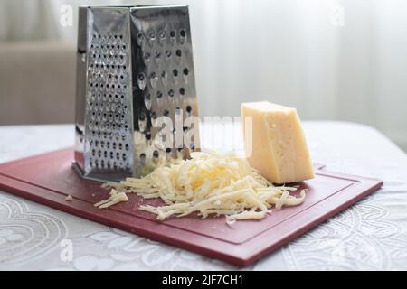 A pile of grated cheese on a plastic board next to a grater Stock Photo