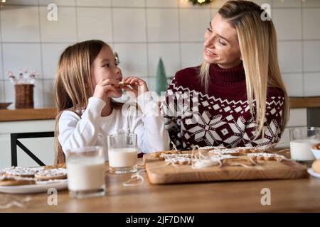 Happy mom and kid daughter having fun eating Christmas cookies. Stock Photo