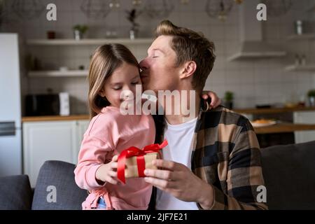 Happy cute child daughter embracing dad making present at home on Fathers Day. Stock Photo