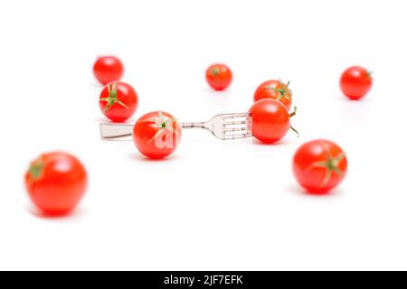 Group of small cocktail tomatoes distributed on a white background. One tomato is pierced with a miniature fork. Stock Photo