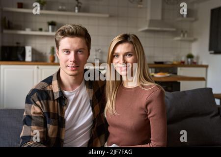 Happy young millennial couple bonding looking at camera sitting on sofa at home. Stock Photo