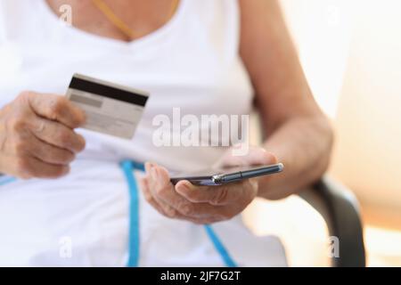 Closeup of elderly woman with hand using a smartphone and holding credit card to pay bills in online stores Stock Photo