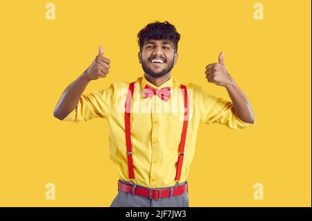 Happy handsome young Indian man in shirt and bow tie showing thumbs up and smiling Stock Photo