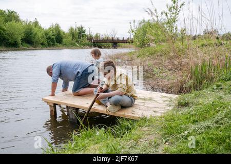 Children with their father on the riverbank playing with water. Stock Photo
