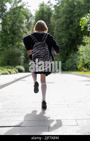 A running girl in a school uniform and a school bag from the back. Stock Photo