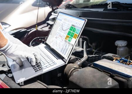 Young Male Mechanic Using Laptop While Examining Car Engine Stock Photo