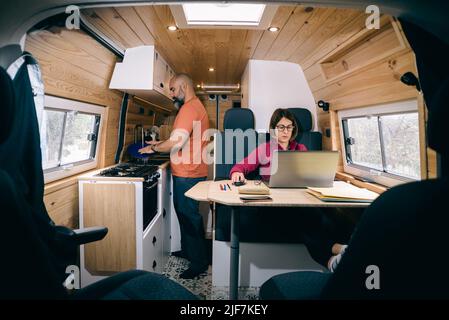 Couple living in a camper van. Woman teleworking. Man washing dishes. Stock Photo