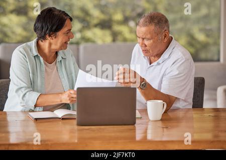 Elderly couple paying bills online on a laptop, sitting by a table at home getting angry, planning retirement. Senior hispanic man and woman having a Stock Photo