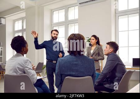 Smart male business coach or team leader talks to employees during work meeting or brainstorming. Stock Photo