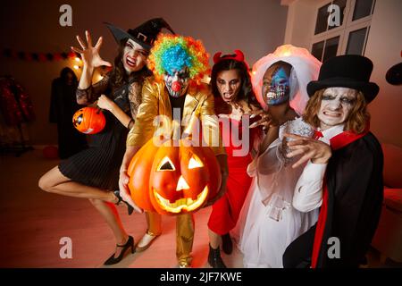 Group of young happy friends in costumes on Halloween having fun at party making scary faces. Stock Photo