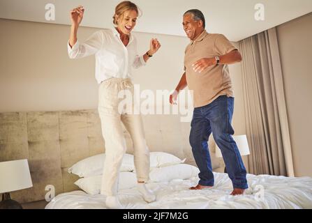 Senior interracial couple jumping on a hotel bed and having fun together. Senior man and woman full of energy and life. They are celebrating and Stock Photo