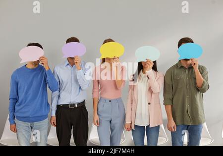 Five young men standing in row hide their faces behind empty colored speech bubbles. Stock Photo