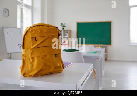 Yellow canvas backpack placed on a student's desk in the classroom at a modern school Stock Photo