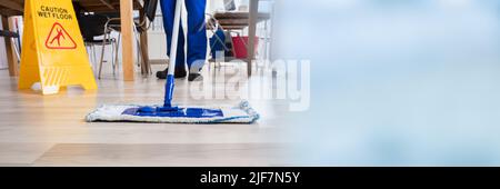 Janitor Cleaning Floor In Front Of Yellow Caution Wet Floor Sign Stock Photo