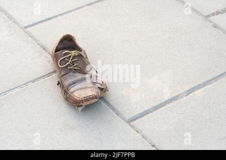 One single lone damaged ripped lost shoe left on a sidewalk, object closeup, nobody. No money, poverty, homelessness simple abstract concept, no peopl Stock Photo