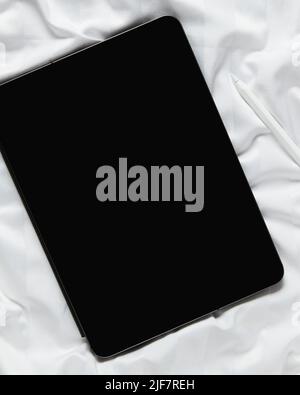 Flat lay top view blank screen digital tablet on white bed. Home office workspace Stock Photo