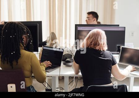 Rear view of young female entrepreneurs working on laptops in tech start-up office Stock Photo