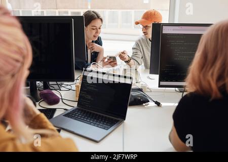 Male and female entrepreneurs discussing over smart phone while working in office Stock Photo