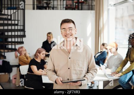 Portrait of smiling male programmer holding tablet PC while standing in office Stock Photo