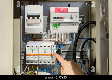 Electrician switches circuit breaker in consumer unit of fuse box and electric meter. Stock Photo