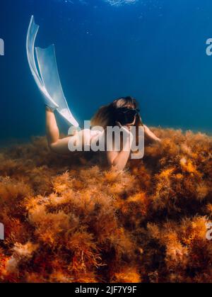 Freediver woman with mask and white fins posing in underwater. Freediving in blue sea Stock Photo