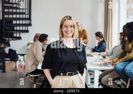 Portrait of smiling young female computer programmer standing with hands in pockets at tech start-up office Stock Photo