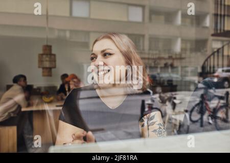 Happy female entrepreneur looking away while sitting in office seen through glass Stock Photo