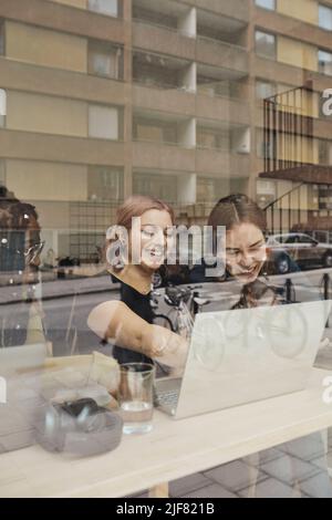 Happy female entrepreneur discussing with colleague over laptop while working in laptop at office Stock Photo