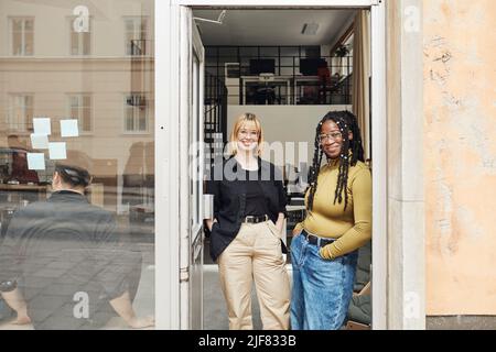 Portrait of young female entrepreneurs with hands in pockets standing at office doorway Stock Photo