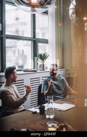 Smiling businessmen gesturing while discussing in meeting room at creative office Stock Photo